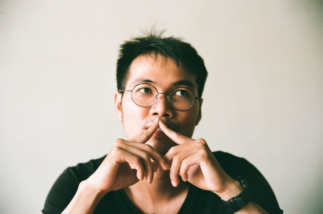 A contemplative young man wearing eyeglasses, captured in a thoughtful pose indoors.