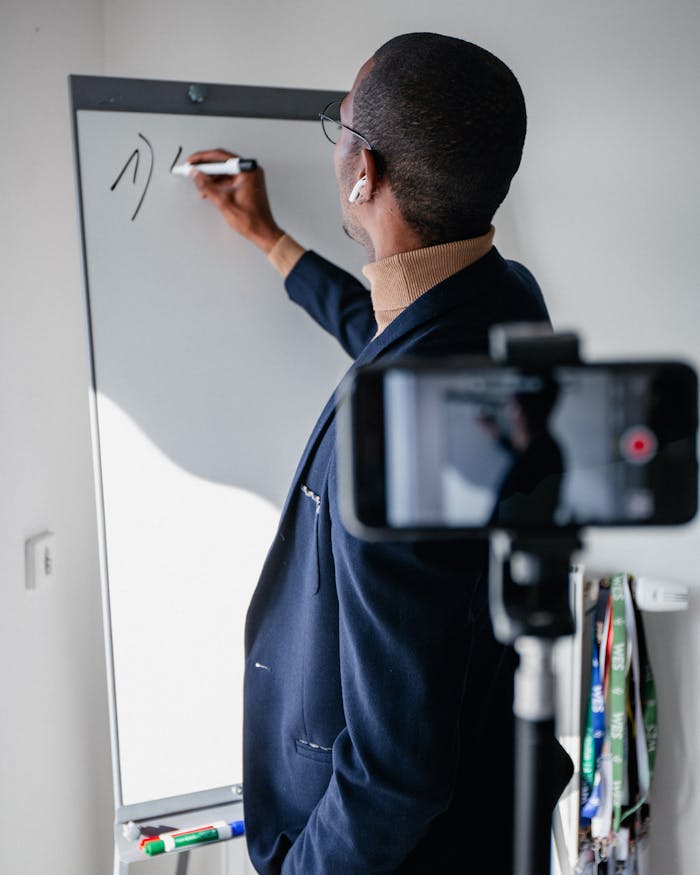 A man teaching remotely using a whiteboard, recorded with a smartphone.