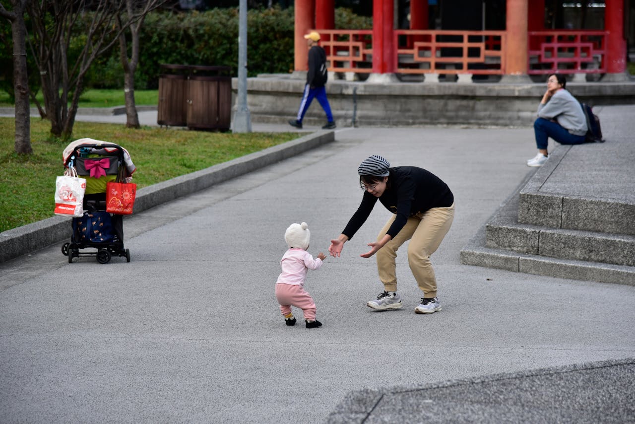 A mother joyfully reaches for her toddler in a city park.