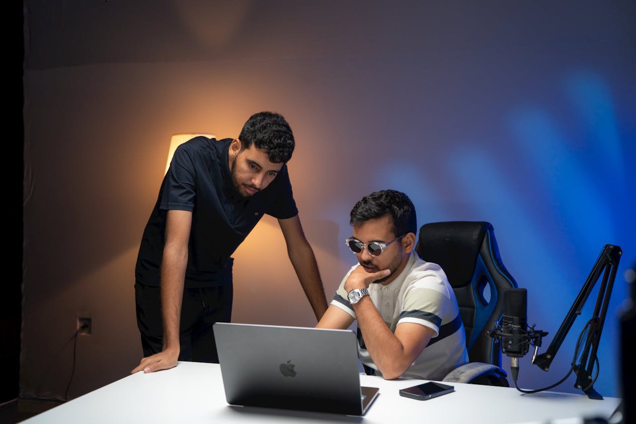 Two men focused on laptop work in an office with blue lighting
