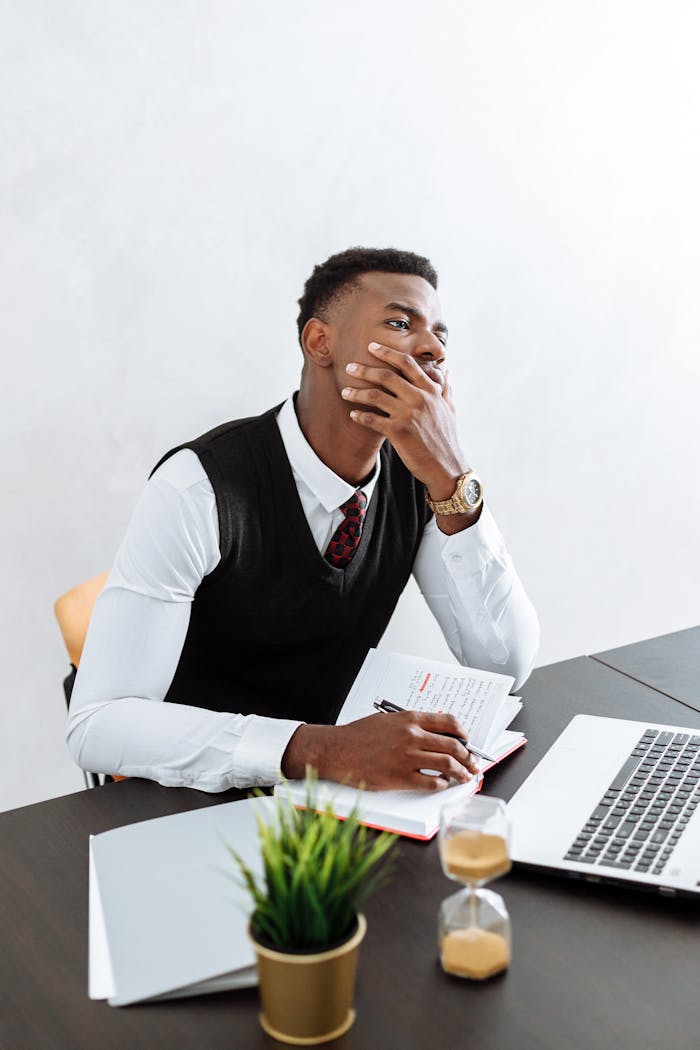 African American businessman pondering ideas at his desk with laptop and hourglass.