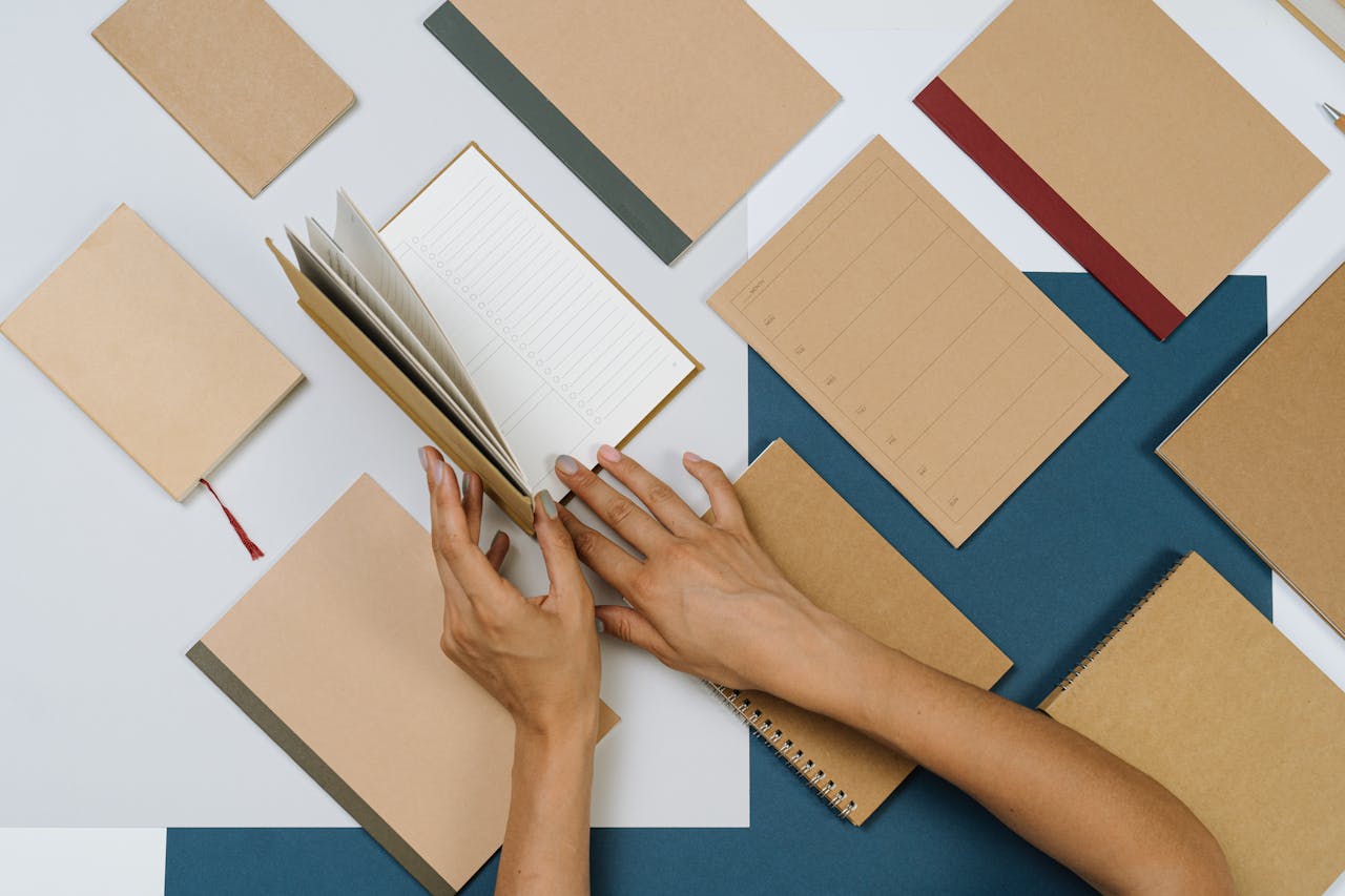 Stylish flatlay of assorted brown stationery items being flipped by hands.