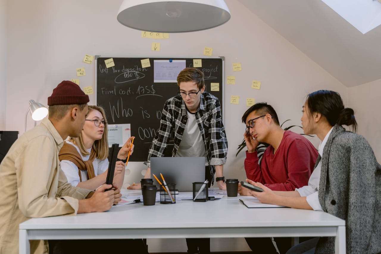 A diverse group of colleagues collaborating in a modern office setting with laptops and sticky notes.